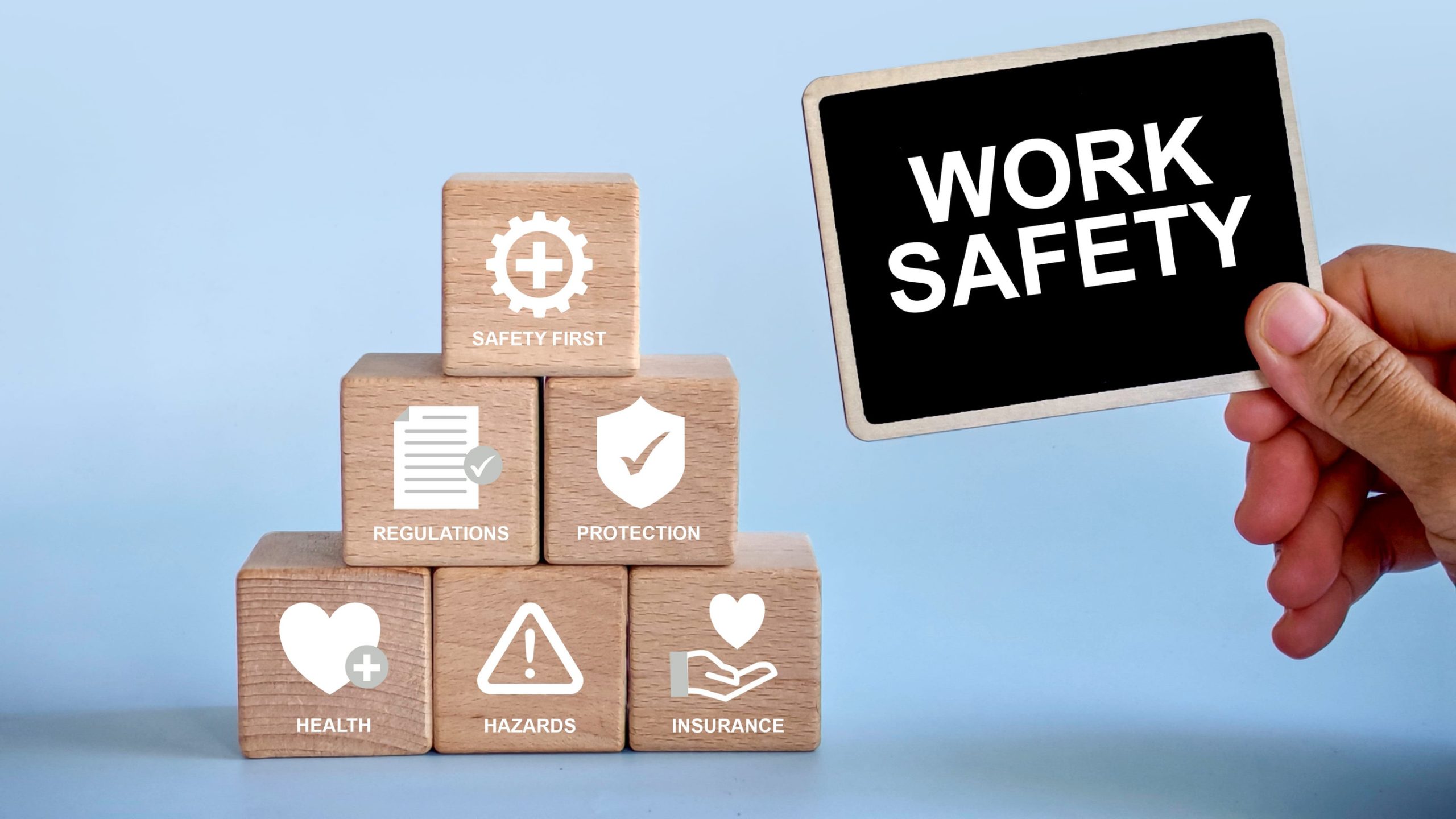 a hand holding notification board written with 'Work safety' with a stack of wooden cube with safety icon beside it.