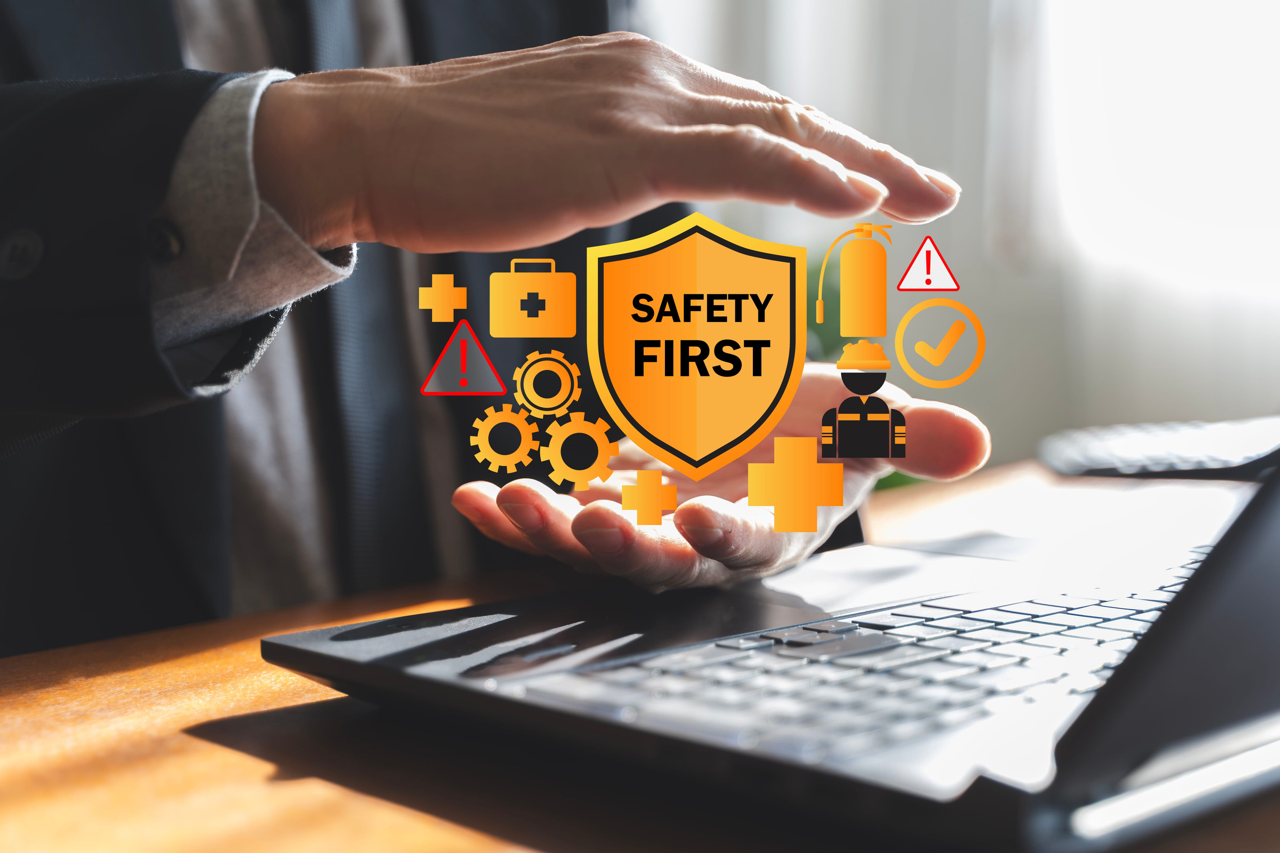 Businessman hands protecting safety first shield icons over laptop, concept of workplace risk management, occupational health, compliance, emergency prevention and safety training.